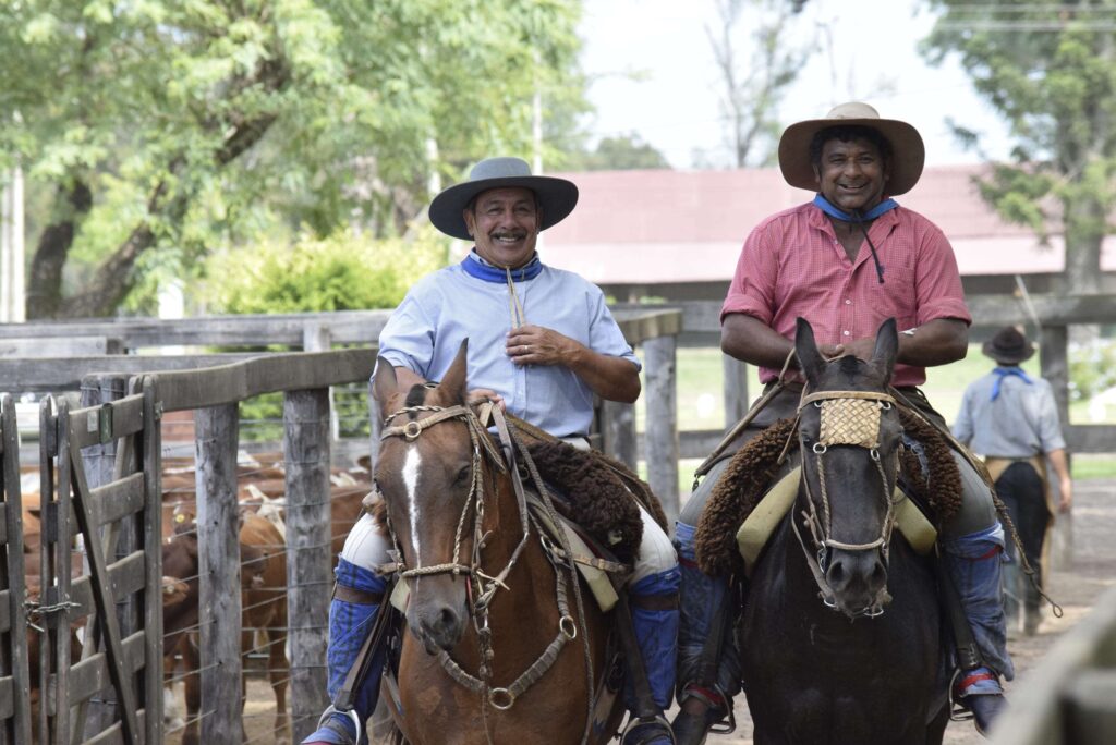 Dos hombres montados a caballo sonríen a la cámara en un corral de madera, representando a los productores locales beneficiarios del modelo de asistencia técnica para ganadería regenerativa en el Gran Chaco.