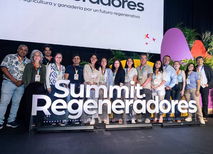 Un grupo de líderes, investigadores y productores posan juntos en el escenario del Summit Regeneradores detrás del letrero oficial del evento, celebrando el lanzamiento de la red de regeneración agroalimentaria en América Latina