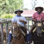 Dos hombres montados a caballo sonríen a la cámara en un corral de madera, representando a los productores locales beneficiarios del modelo de asistencia técnica para ganadería regenerativa en el Gran Chaco.