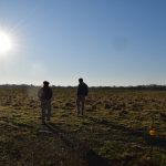 Vista a contraluz de dos personas caminando por un lote ganadero de la finca Los Tres Quebrachos bajo un sol radiante e intenso. La imagen ilustra las condiciones de calor extremo del Gran Chaco argentino y las estrategias adaptativas frente al clima.