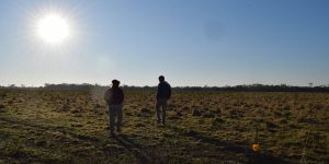 Vista a contraluz de dos personas caminando por un lote ganadero de la finca Los Tres Quebrachos bajo un sol radiante e intenso. La imagen ilustra las condiciones de calor extremo del Gran Chaco argentino y las estrategias adaptativas frente al clima.